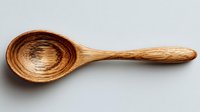 Handcrafted wooden spoon with natural grain pattern on neutral background, showcasing rustic kitchen utensil for cooking and serving.