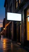 Blank white illuminated storefront sign on brick building at dusk with wet street reflections for business branding and advertising mockup.