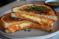 Grilled cheese sandwich with melted cheddar and mozzarella on toasted white bread, garnished with fresh herbs, cut diagonally to show gooey cheese pull texture.