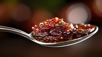 Sweet and savory fig jam with crushed walnuts on silver spoon, dark background with bokeh effect creates gourmet food styling atmosphere.