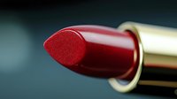 Close-up macro shot of classic red lipstick bullet showing rich texture and glossy finish against dark background, highlighting cosmetic product detail.