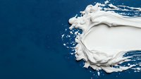 White cream splash on dark blue background with dynamic motion and swirling texture creates dramatic contrast, suitable for cosmetic and skincare advertising.