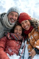 Happy multiethnic family with child enjoying winter vacation together in snowy mountains wearing warm knitted hats and jackets smiling outdoors.