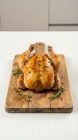 Whole roasted chicken with golden crispy skin, garnished with fresh thyme and rosemary on a rustic wooden cutting board.