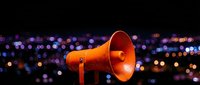 Orange megaphone against blurred city lights at night creates dramatic communication concept for marketing and announcement campaigns.