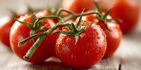 Fresh ripe red tomatoes on vine with water droplets on wooden surface for healthy cooking and organic food preparation.