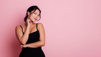 Young Asian woman in black dress posing thoughtfully against pink background, perfect for beauty, fashion, and lifestyle marketing.