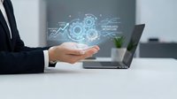 Business professional presenting digital technology innovation with holographic gears and data analytics above open palm in modern office workspace.