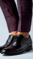 Elegant black leather oxford shoes with burgundy plaid pants, showcasing modern men's fashion detail. Close-up view emphasizes polished leather texture and classic design.