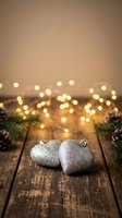 Silver glittery Christmas ornaments on rustic wooden table with warm fairy lights and pine branches creating festive holiday atmosphere for seasonal decorating.