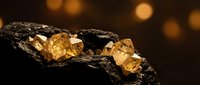 Raw gold nuggets embedded in dark mineral ore rock with warm bokeh lighting background for mining and precious metals concepts.
