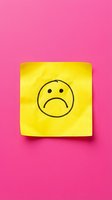 Yellow sticky note with sad face emoji on bright pink background for mental health awareness and emotional expression concepts.