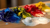 Colorful oil paint blobs on artist palette with brush, featuring vibrant blue, yellow, red and white colors mixed for creative artwork and painting projects.