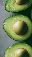 Fresh cut avocado halves with water drops on dark background, macro shot showing creamy texture and natural pit. Healthy organic food photography.