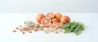 Natural sources of folic acid including eggs, grapefruit, nuts, seeds and leafy greens arranged on white background for healthy nutrition and pregnancy diet.