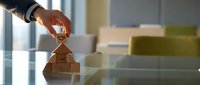 Male hand placing wooden building blocks in stacking formation on glass surface, representing business growth, real estate development, and strategic planning for corporate success.