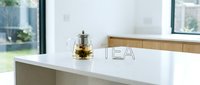Glass teapot with blooming flower tea on a white kitchen counter, modern interior background with large windows and natural light.
