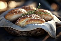 Fresh baked artisanal bread rolls with crispy crust, sea salt and rosemary sprigs served in rustic wicker basket with white cloth napkin on dark background.