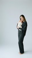 Young Caucasian mother in dark pajamas tenderly holding newborn baby against chest, bonding moment on white background for parenting content.
