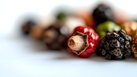 Colorful peppercorns macro shot showing red, black, and green varieties with selective focus on foreground spice against white background. Perfect for culinary designs.