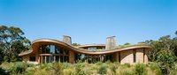 Modern curved roof luxury home with large windows surrounded by native landscaping under clear blue sky for architectural design projects.