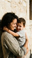 Middle-aged Hispanic mother embracing young son against rustic stone wall in warm sunlight showing maternal love and family bonding moments.
