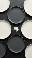 Overhead view of empty ceramic plates in black and cream arranged in pattern on dark slate surface with white orchid flower, suitable for tableware, dining, and restaurant design projects.