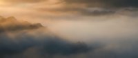 Dramatic storm clouds with golden sunlight breaking through misty atmosphere creating moody sky for weather and climate concepts.