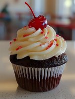 Chocolate cupcake with vanilla frosting topped with maraschino cherry and red sprinkles on kitchen counter for bakery dessert menu or celebration treats.