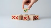 Hand placing wooden cube with green checkmark above row of blocks with red X marks representing choice between success and failure in business decisions.