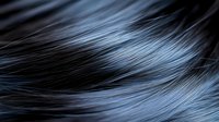 Close-up of lustrous dark hair strands with blue highlights flowing in smooth waves, showcasing natural texture and shine for beauty and haircare concepts.