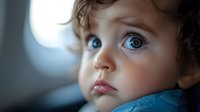 Toddler with curly brown hair and blue eyes wearing blue clothing, looking upward with wonder and curiosity in soft natural light.