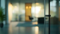 Blurred modern office interior with glass walls and warm lighting creates atmospheric business environment with bokeh effect and reflective surfaces.