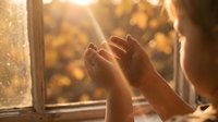 Woman hands reaching toward warm sunlight streaming through window with golden autumn bokeh background creating peaceful morning meditation moment.