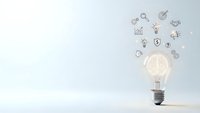 Glowing light bulb with business icons floating above on clean white background representing innovation and creative thinking for presentations.