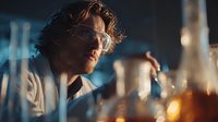 Male scientist with curly hair conducting chemical research in modern laboratory with glassware and equipment for pharmaceutical development and analysis.