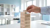 Businessman in light blue shirt placing wooden block on tower stack, symbolizing business growth, strategy, and risk management in modern office environment.