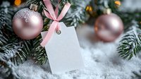 Elegant Christmas composition with pink ornaments, blank gift tag with ribbon, and snow-covered evergreen branches for holiday greeting cards and festive designs.