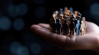Small wooden figures standing in group formation on open palm against dark background with bokeh lights, representing unity and leadership concept.