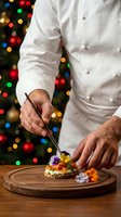 Professional chef plating gourmet appetizer with edible flowers on wooden board against festive Christmas lights background for holiday catering menu.