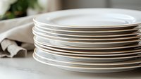 Stack of clean white ceramic dinner plates on light gray tablecloth with soft natural lighting and shallow depth of field, creating minimalist dining atmosphere.