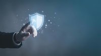 Businessman hand touching glowing shield icon with sparkles on blue background representing cybersecurity protection and data safety concepts.