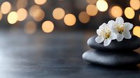 Zen spa stones with white cherry blossoms and warm bokeh lights creating peaceful meditation atmosphere for wellness and relaxation treatments.