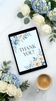 Digital tablet displaying thank you card with floral design surrounded by blue hydrangeas, white roses and eucalyptus leaves with coffee cup on marble surface.