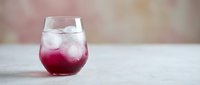 Refreshing layered cocktail with purple gradient and ice cubes in stemless glass on marble surface for beverage photography and restaurant marketing.
