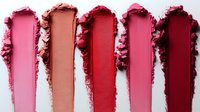 Crushed makeup powder swatches in shades of pink and red on white background, showing texture and pigmentation of cosmetic products for beauty industry use.