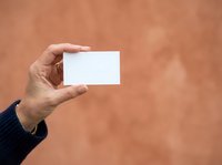 Male hand holding blank white business card against terracotta textured wall background, suitable for branding, corporate identity, and marketing mockup designs.