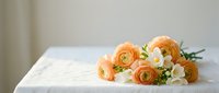 Orange ranunculus and white flowers bouquet lying on white marble surface with soft natural lighting for wedding decor and floral arrangements.