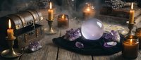 Mystical fortune telling setup with crystal ball, amethyst crystals, burning candles and ancient books on wooden table for spiritual divination practices.