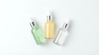 Three cosmetic bottles with silver pumps containing green, yellow and clear liquids on white background for skincare product mockup.